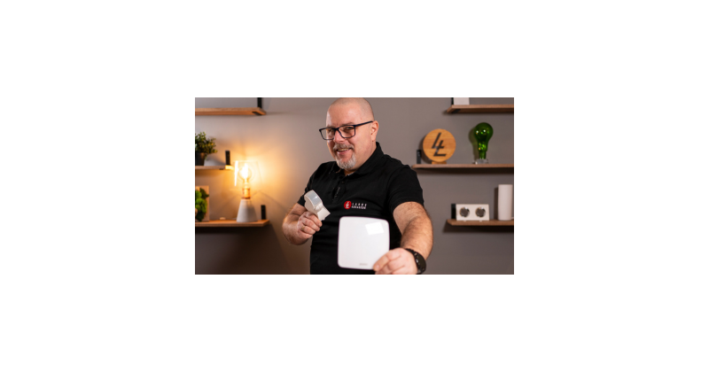Baner promujący webinar „DALI bez tajemnic” z datą 29.04.2026 o godzinie 12:00. Na zdjęciu uśmiechnięty mężczyzna w okularach prezentuje dwa białe urządzenia do sterowania oświetleniem na tle warsztatowym.